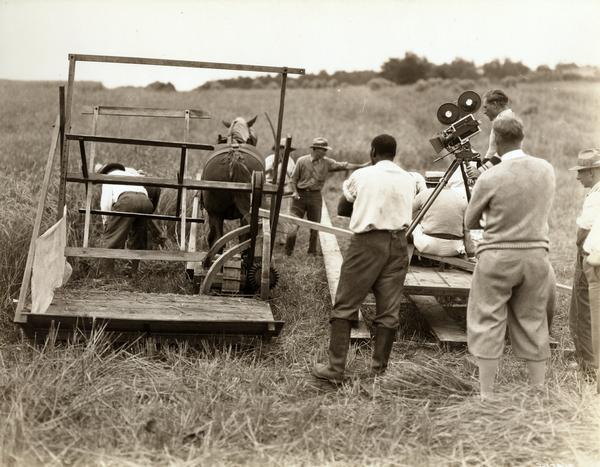 Film crew setting up a scene in which actors playing the parts of  Cyrus McCormick and his slave Jo Anderson operate a replica of McCormick's reaper of 1831. The scene was part of a feature length motion picture titled "Romance of the Reaper." The film was produced by the International Harvester Company to celebrate the 100 year anniversary of the invention of the reaper, also known as the "reaper centennial."