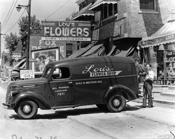 Man loading a floral arrangement into an International model D-2 panel delivery truck for Lou's Flower shop.