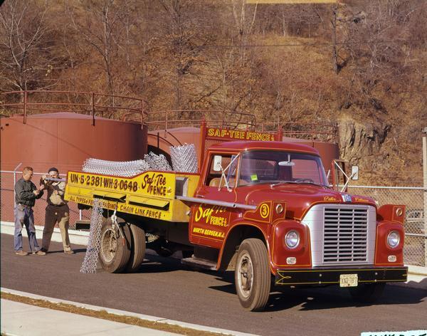 Color photograph of an International Loadstar 1600 truck with chain link fence pieces in the bed. The truck was owned by Saf-Tee Fence, Inc., of New Jersey. Storage tanks are in the background.