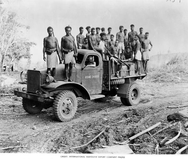 Men, natives of the Solomon Islands, standing on a U.S. Marine Corps truck made by International Harvester. Some of the men are holding rifles.