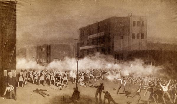 Photograph of a painting depicting a confrontation between police and protesters at the Haymarket in Chicago. Smoke from an explosion drifts in the background as bodies lie on the ground dead or wounded. Thousands of protesters had gathered in response to the killing of two McCormick reaper factory workers on the previous day. The workers had been killed by police in a confrontation between union workers and their replacements.
