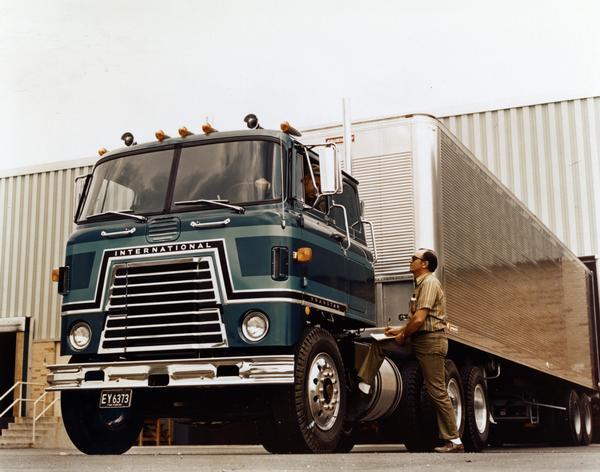 Color photograph of a loading dock worker talking to a driver sitting in the cab of an International Transtar semi-truck.