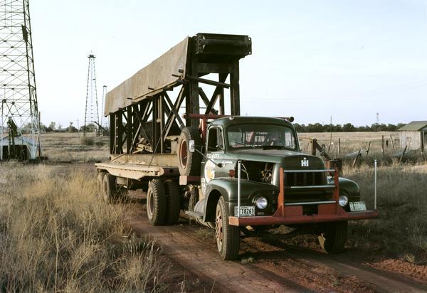 Color photograph of an International model R-202 oil field truck owned by M.R. Dixon. The truck is parked in an oil field with oil derricks in the background.