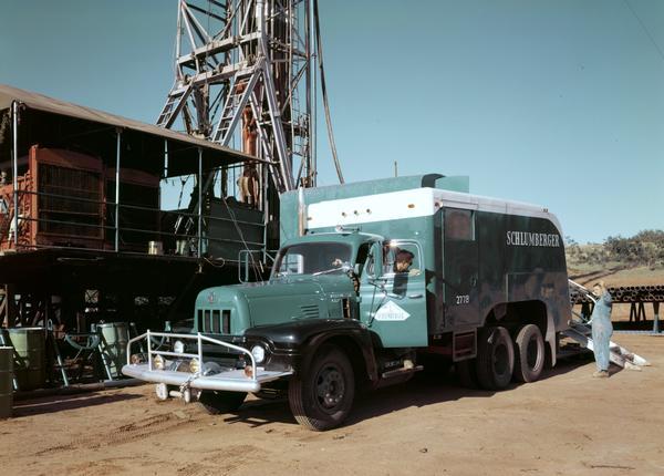 Color photograph of workers positioning an International model RF-190 oil field truck near an oil derrick. The truck was owned by Schlumberger Well Servicing.