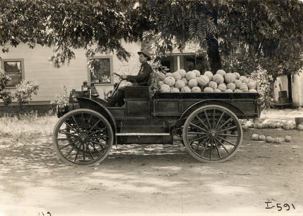 Man sitting in the driver's seat of an International Model M truck loaded with pumpkins.