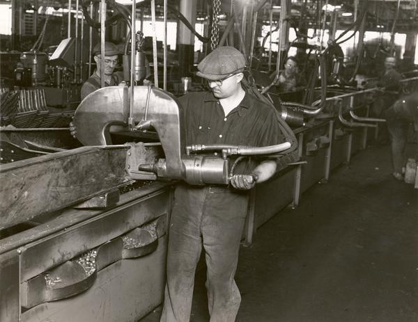 Factory worker using a Hannifin hydraulic riveter on a frame assembly line at International Harvester's Fort Wayne Works.