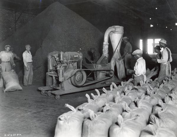 A group of workers grinding fertilizer with a power hammer mill.  Original captions reads: "The Fish Meal Company of Fernandina, Florida, uses this International Model 200 power unit and International Harvester Model 1-B hammer mill for grinding fish for fertilizer. "