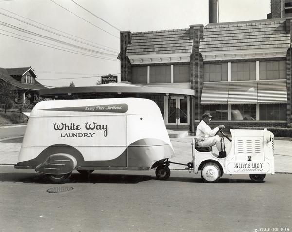 Employee of White Way Laundry pulling a trailer with a Hebard shop mule on a suburban street. The shop mule is powered by an International P-12 engine. A slogan on the trailer reads: "Every Piece Sterilized."