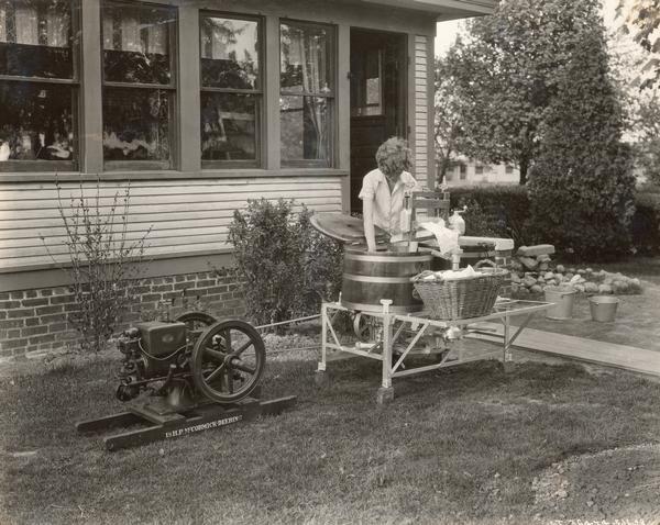 Woman washing clothes with a washing machine powered by a a McCormick-Deering 1 1/2 HP engine.