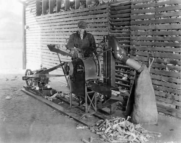 Farmer operating a McCormick-Deering corn sheller powered by a portable engine.