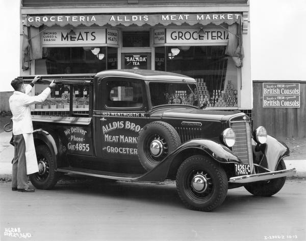 Grocer closing the canopy on an International C-1 delivery truck owned by Alldis Brothers Meat Market and Groceries of Hamilton, Ontario, Canada.