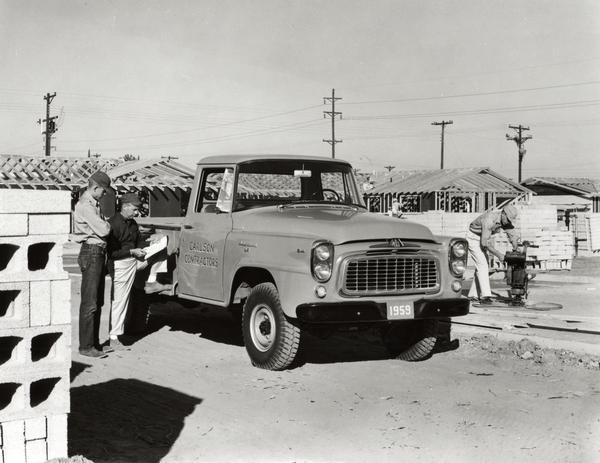 Men working around an International pickup truck parked at a construction site. The truck, possibly a B-120 or B-130, was owned by Carson Contractors.