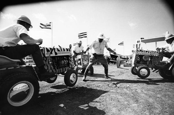 Men riding Cub Cadet lawn tractors in International Harvester's "wild-animal" act at the Farm Progress Show in Farmer City, Iowa. Three International Harvester salesmen piloted the jungle cat Cub Cadet tractors and George Mann, a professional actor, played the part of "Fisbee" the "hapless animal trainer".