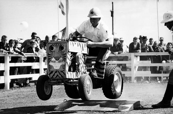 Man riding a Cub Cadet lawn tractor in International Harvester's "wild-animal" act at the Farm Progress Show in Farmer City, Iowa. Three International Harvester salesmen piloted the jungle cat Cub Cadet tractors and George Mann, a professional actor, played the part of "Fisbee" the "hapless animal trainer".