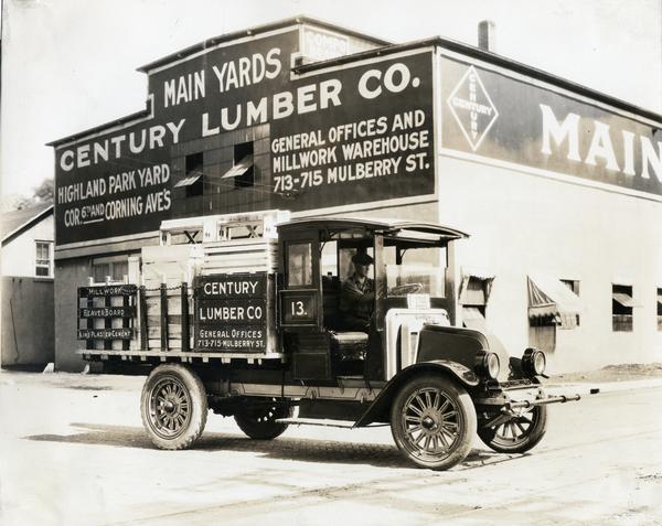 International model 31 truck carrying lumber for Century Lumber Co. The truck is parked outside the company's warehouse. A man is sitting in the driver's seat.