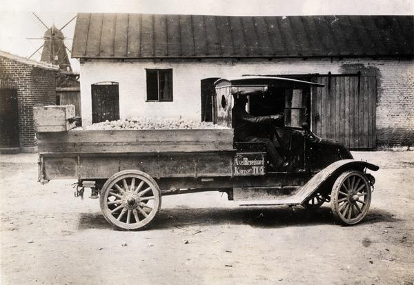 International model 31 truck owned by Axel Broegaard, an egg buyer, in Karise, Denmark. The truck was carrying 22,000 eggs and was bought from H.C. Peterson and Co. in Copenhagen, Denmark. The photograph was provided by International Harvester Company in Hamburg, Germany. A windmill is in the background behind buildings.