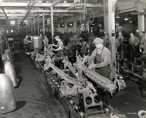 Workers on an assembly line at an International Harvester factory. The original caption reads: "assembling 57mm gun carriages."