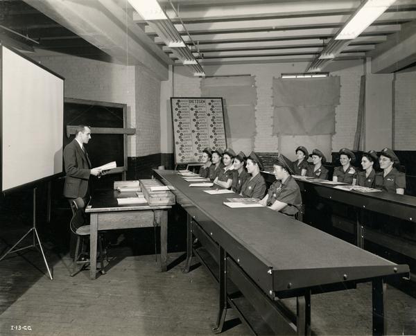A group of recently hired factory female workers receive their first day of training at an International Harvester factory. The factory was responsible for production of aerial torpedoes for the U.S. Military. The women are receiving a refresher course in mathematics with an emphasis on decimal fractions. They are also becoming familiar with shop tools and equipment.
