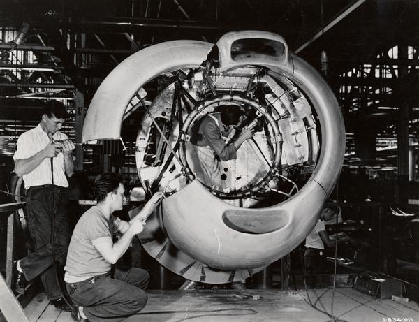 Workers drilling on a section of a military airplane cowling at an International Harvester factory.