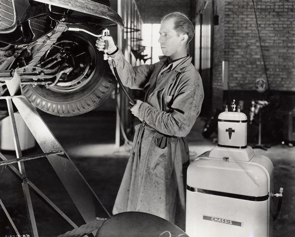Mechanic reconditioning a used International truck at an International Harvester dealership(?). The man is applying pressure lubrication.