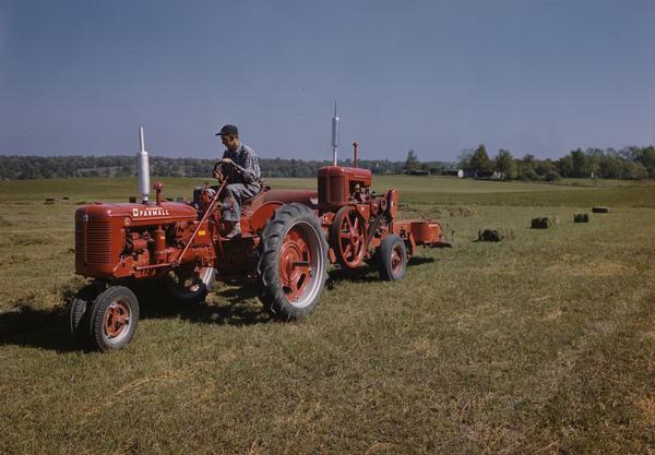 Color photograph of a farmer baling hay with a Farmall C tractor and baler.