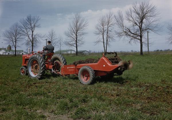 Farmer spreading manure in a field with a Farmall H tractor and manure spreader (possibly a model 100).