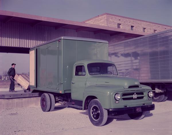 Color photograph of a man loading cargo into the 12-foot Freuhauf van body of a R-150 International truck.