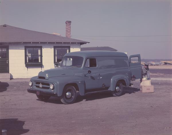 Color photograph of an International R-110 panel truck delivering supplies outside an airport restaurant.  A delivery man is unloading eggs and other items.