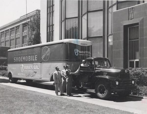Businessmen standing next to an International L-185 truck owned by the Max Branovan Shoe Company. The trailer is labeled "A. O. Smith Company Shoemobile".