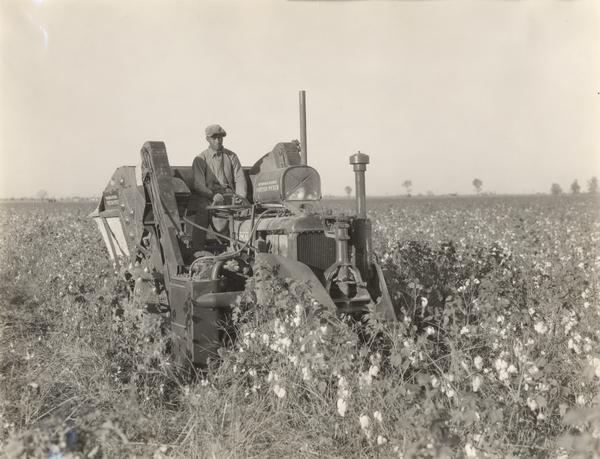 African American man operating an experimental two-row cotton picker in a field.