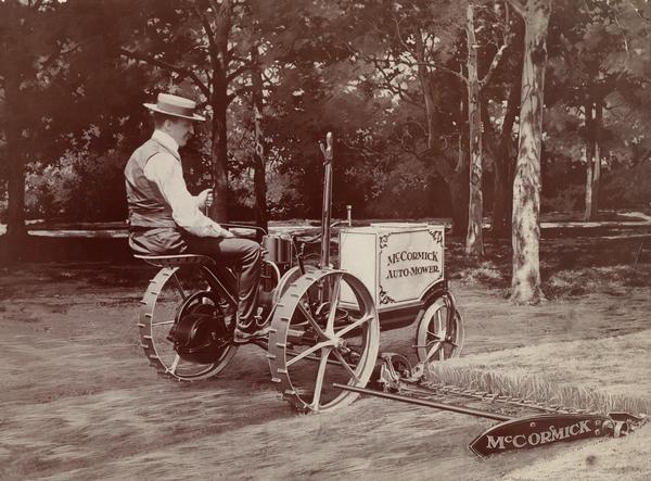 A man demonstrating the McMormick "Auto-Mower". The image appears to have been retouched by an artist. The Auto-Mower was an experimental engine powered mower that won first prize at the exposition. This is one of two Auto-Mowers produced by the company. This machine had a single-cylinder engine. The other machine had a two-cylinder engine. The photograph was likely taken at the Paris Exposition in France in 1900.