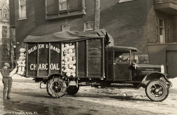 Man delivering a bag of "Beaver" brand charcoal from an International SF-34 truck. The man worked for the Charcoal Supply Company of Quebec, Canada.