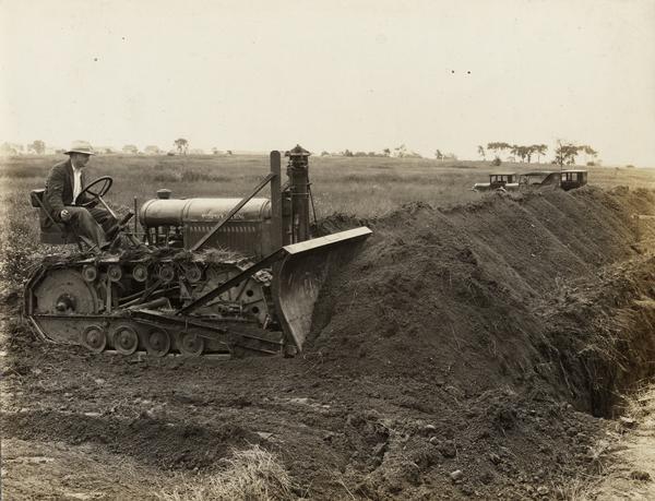 Man bulldozing a pile of dirt with a McCormick-Deering crawler tractor with an attached blade. The blade was manufactured by the Frank G. Hough Company.