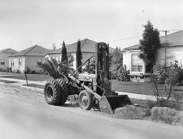 Man working on a suburban road with an International ID-6 and attached loader. The loader was manufactured by the Frank G. Hough Company.