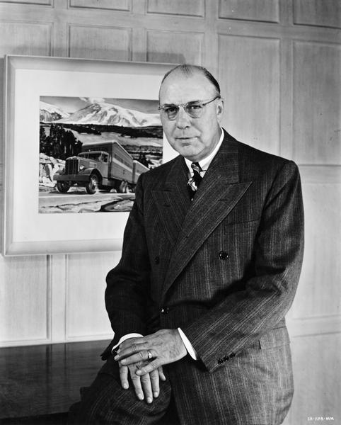 Portrait of John L. McCaffrey, wearing eyeglasses, posing while sitting on a desk or table. He was president of International Harvester Company from 1946-1958.