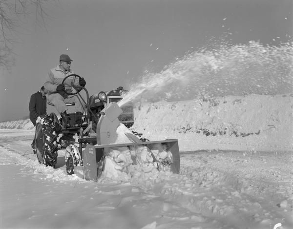 Man driving a Farmall Cub equipped with Danco snowblower clearing a roadway of snow.