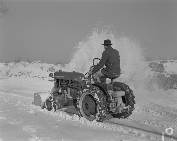 Man driving Farmall Cub equipped with Danco snowblower clearing a roadway of snow.