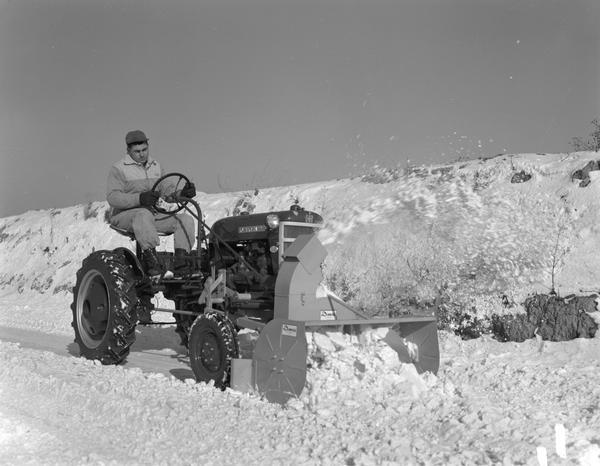 Man driving a Farmall Cub equipped with a Danco snowblower removing snow from a roadway.