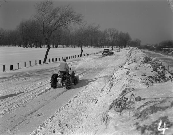 A man driving a Farmall Cub with Danco snowblower clearing a road of snow.