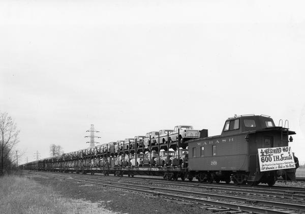 A large shipment of newly built International Scouts headed West.   Sign on the front of the train reads: "Westward Ho!  600 IH Scouts for Phoenix, Los Angeles, Oakland. 'All America' is Sold on the Scout."