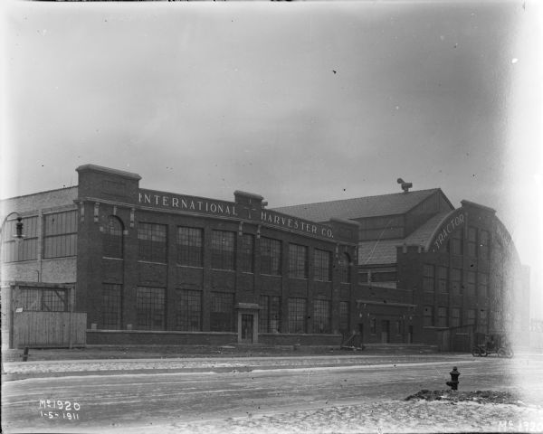 Exterior of International Harvester's Tractor Works. The Tractor Works plant was in operation from 1910-1972, and manufactured tractors and construction equipment.  A car is parked in front of the building.