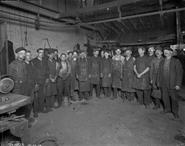 A group of employees posing in one of International Harvester's factories, most likely Osborne Works (later known as Auburn Works) in Auburn, New York. Many of the men are wearing aprons, and all are covered in a dark substance, possibly soot.