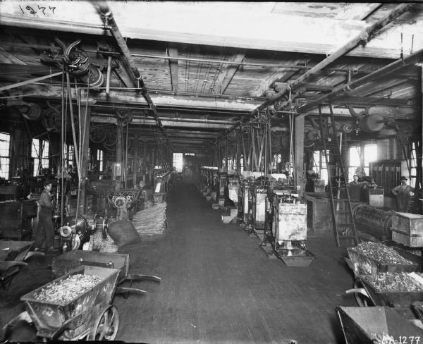 A large room with manufacturing equipment at the McCormick Harvesting Machine Company's factory ("reaper works") in Chicago.  Men in work clothes are at some of the machines.  Various small metal parts are in wheelbarrows and piled on the floor.