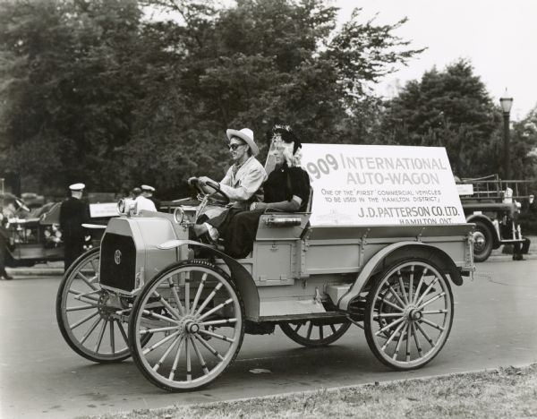 Two men in costumes drive an "antique" 1909 International Auto Wagon in a parade in Hamilton, Ontario. One man appears to be dressed in women's clothing and a wig.