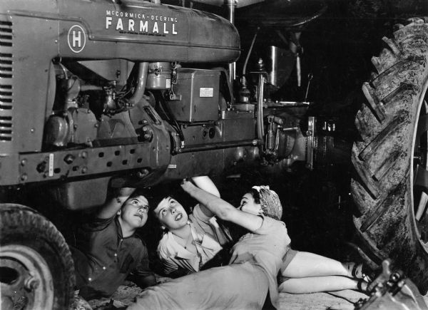 Three women work under a Farmall H tractor. International Harvester's "Tractorette" program was intended to teach women to operate and maintain tractors while their husbands were serving in the military during World War II.