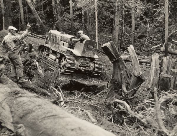 Men using a McCormick-Deering TracTractor (crawler tractor) to pull tree stumps from the ground. The men may be clearing the way for a road.