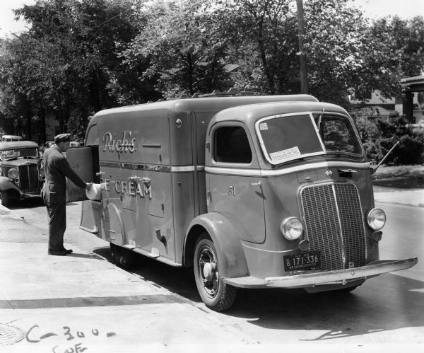 A man is removing a tub of ice cream from a truck that reads "Rich's Ice Cream." The truck is an International C-300 COE (cab over engine). A small sign in the windshield advertises a church's orphan picnic.