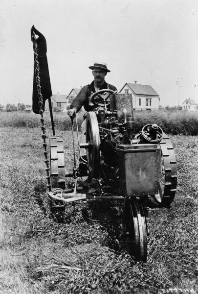 Man operating an Auto-Mower in a field. The Auto-Mower was an experimental gas powered mowing machine. This version was likely produced by the Deering Harvester Company.