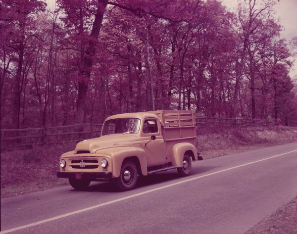 Color photograph of an International R-110 Truck with pickup body and "Ad-A-Rak" with stock extensions. The truck is on a rural highway.