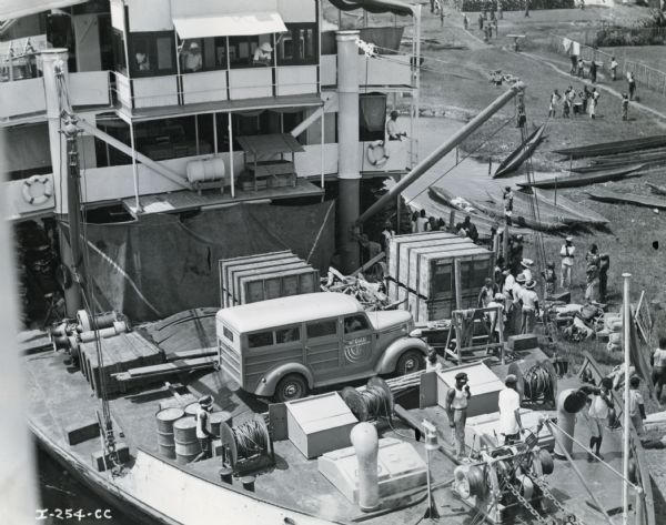 Elevated view of men unloading trucks and equipment from a ship shortly after arrival in the African Congo. The equipment was used by Commander Atillio Gatti on his tenth African expedition. The expedition was sponsored by the International Harvester Company. An International D-2 station wagon ("woody") is on the deck of the ship.